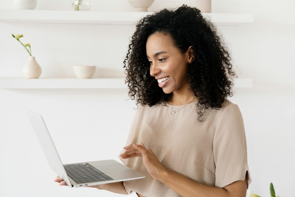 Woman standing and holding her laptop in her hand. She is smiling.